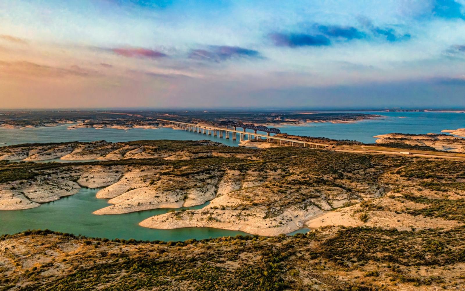 Aerial view of Amistad Reservoir with the Governor's Landing Bridge in Del Rio, Texas at sunset. Fed by the Rio Grande, Devils River, and Pecos River, water levels at Lake Amistad have been low for over a decade.