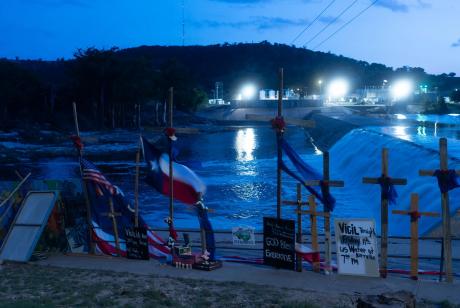 Crosses honoring the victims of the Hill Country floods, seen on July 11, 2025, were erected by artist Roberto Marquez next to the Guadalupe River in Guadalupe Park. Search efforts were suspended Sunday amid new warnings of potential flash flooding in the region. Storms on Sunday brought more floods across Central and North Texas, leading to rescues and evacuations in several counties. Credit: